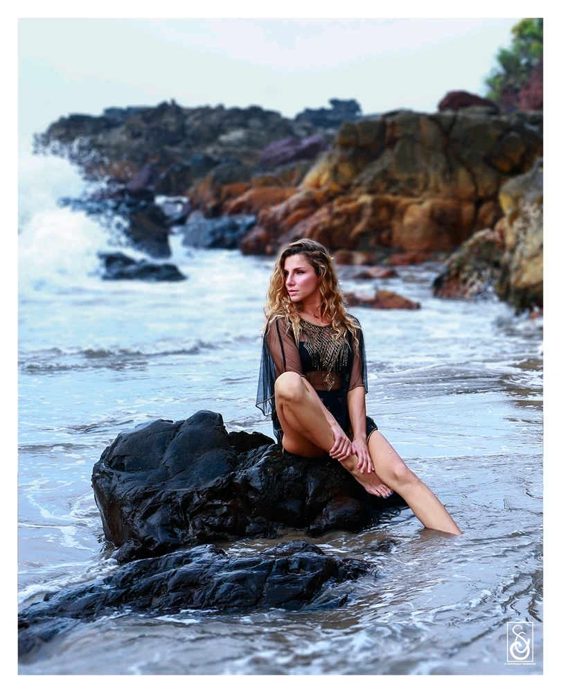 A beautiful girl sitting on a rock by the beach.