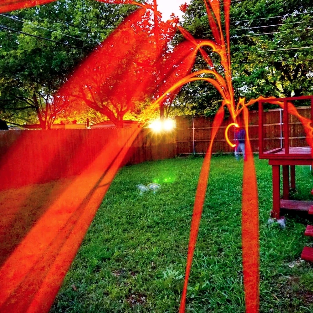 A back yard with a fence and a wooden structure, many red streaks fly toward the camera.