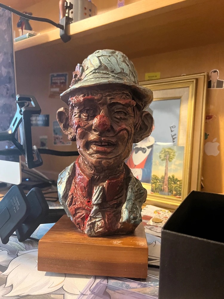 A bust of a tramp clown wearing a hat sits on a desk. 