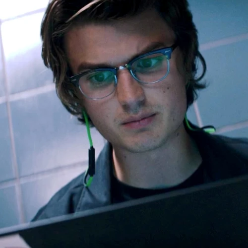 Keys from Free Guy who is played by Joe Keery sat in the bathroom stall on his laptop