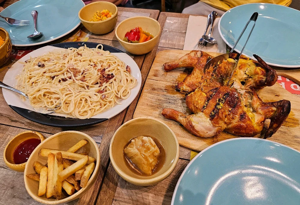 A wooden table filled with food: vegetables, carbonara, grilled chicken, fries, and mashed potato.