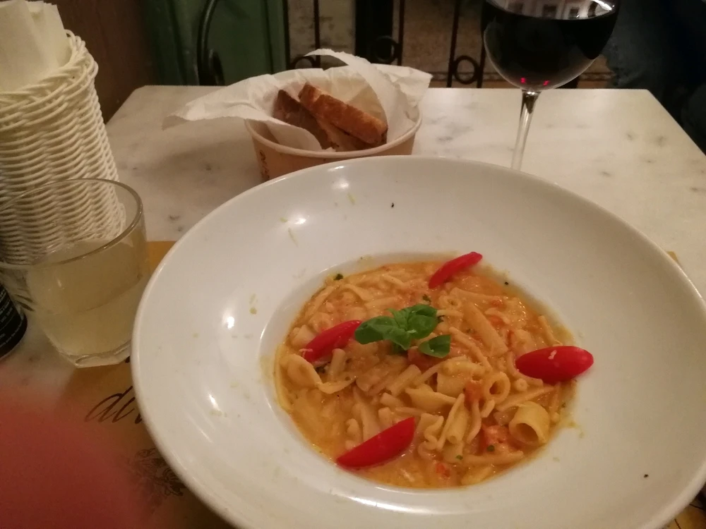 Picture of tasty pasta with cheese and tomatoes, a glass of wine, soda and a basket with bread. 