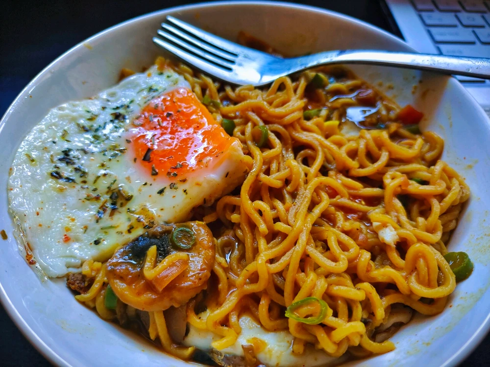 A hot bowl of ramen, with a sunny side up egg and spices. The ramme has various vegetables in it and looks really tasty.