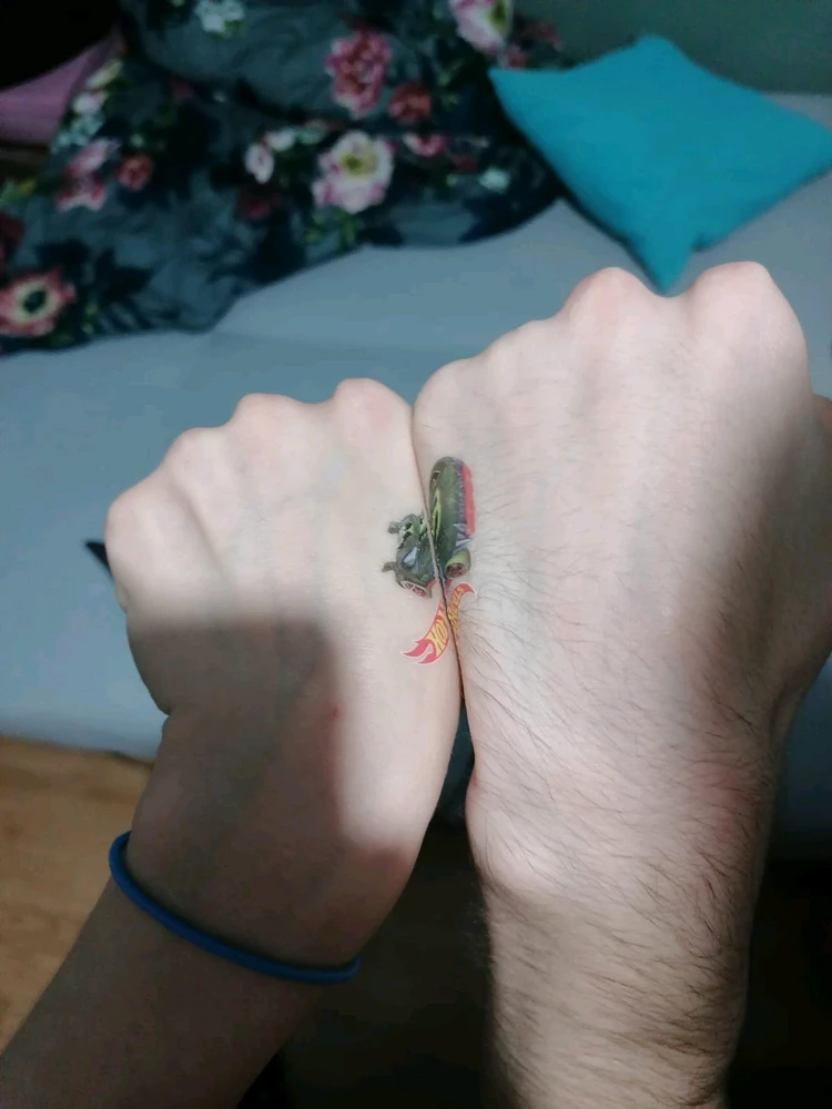 Two fists next to each other. In both of them is a picture of half a hotwheels car. Both fists together show the whole car. 