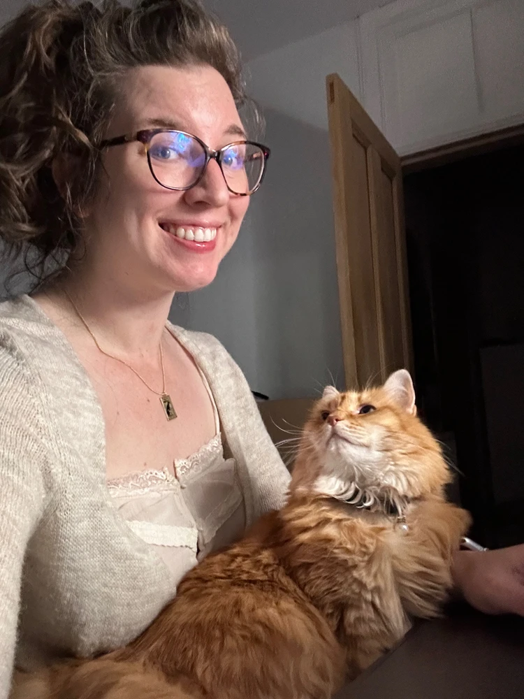 A ginger long-haired floofy cat gazes adoringly up at her person from said person’s lap. Whilst  person was trying to work