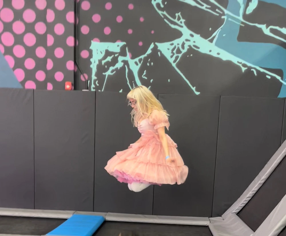 Blonde in a pink dress jumping on a trampoline 