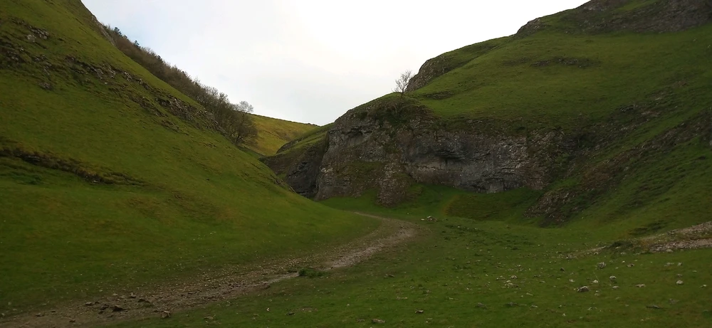Lush green gorge with rugged rocky sides mixed with greenery. A path winds through the middle into the distance.