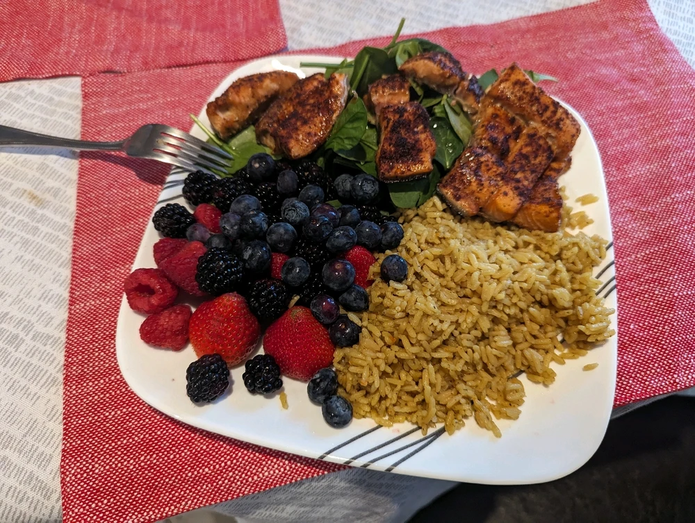 Seasoned salmon on top of baby spinach with chicken fried rice, blueberries, blackberries, strawberries and raspberries 