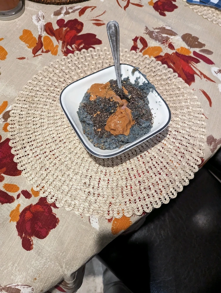 Kodiak blueberry oatmeal with, liquid egg whites, chia seeds and peanut butter with a spoon in the middle in a bowl