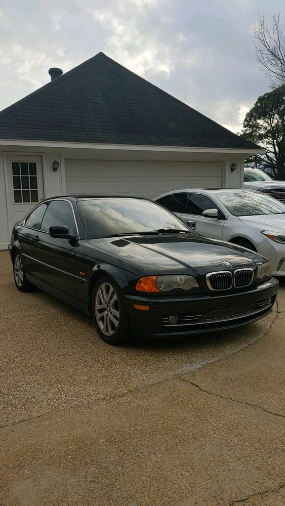 black bmw e46 sitting in a driveway under a cloudy sky.