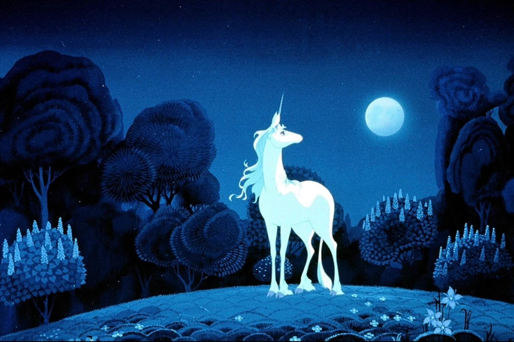 Screenshot from “The Last Unicorn,” featuring the (currently) unnamed unicorn in a moonlit landscape of deep twilight blue. 