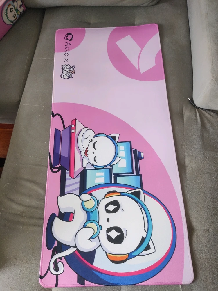 A pink large deskpad with a white cat playing games with a controller/headphones and a small white cat sleeping