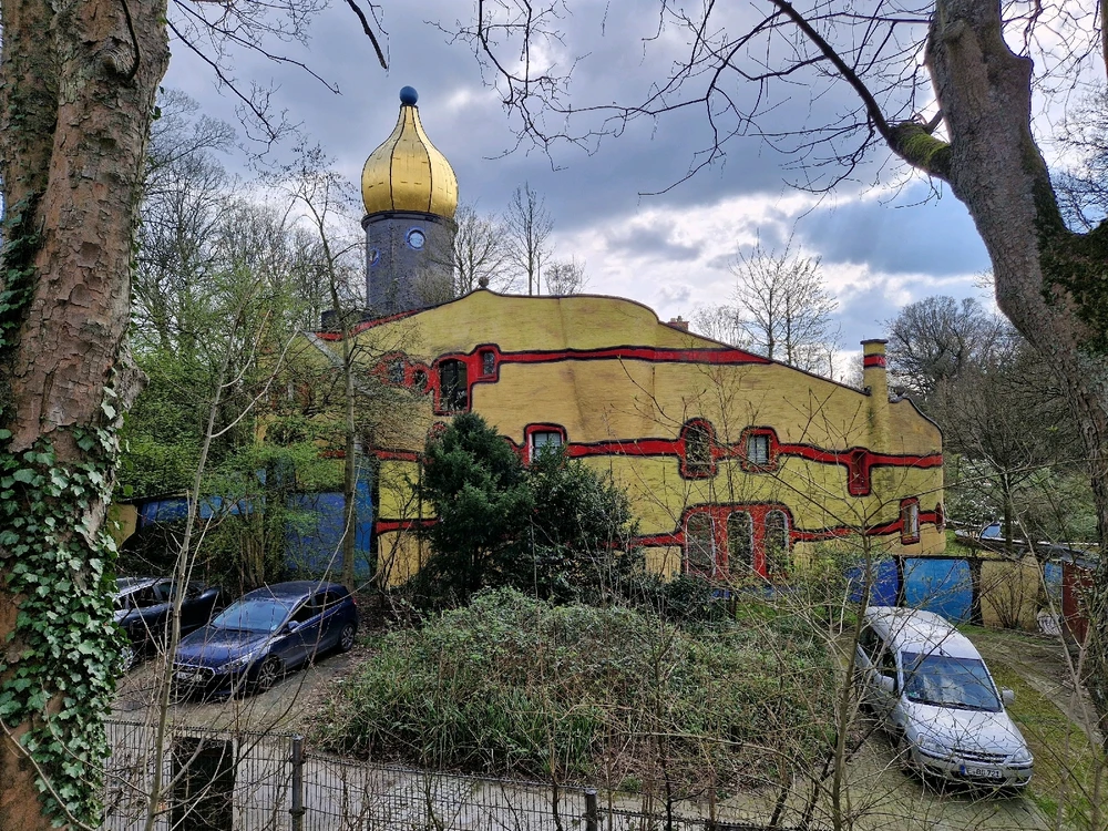 Ein Haus mit untypischer Form, verstreut platzierten Fenstern, rot-gelb gestreifter Fassade und goldener Kuppel