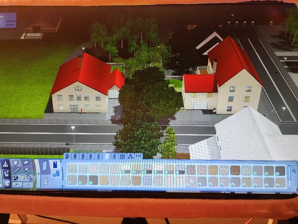 Two similar houses stand side by side. They are tan with red roofs with lush back yards and trees surrounding them. 