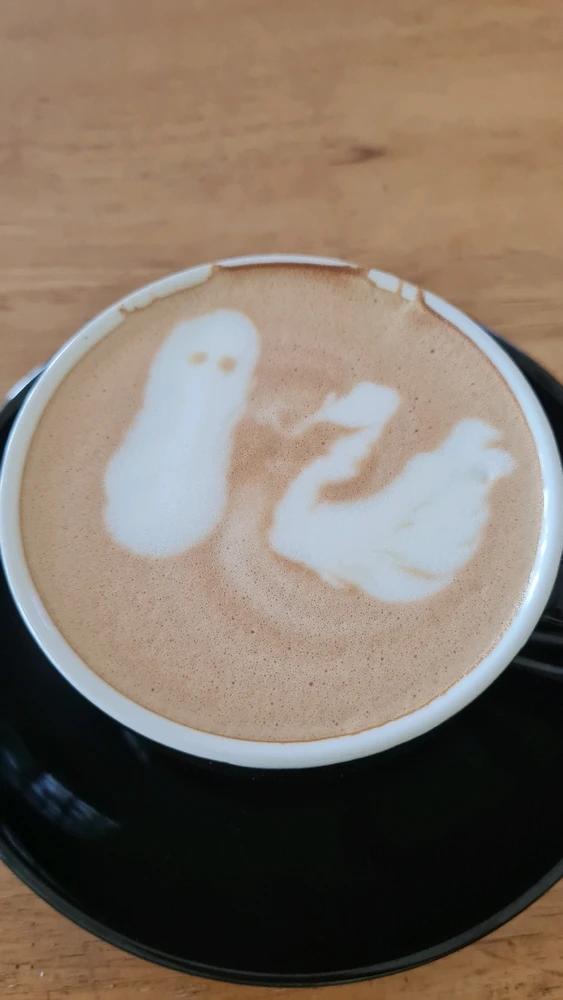 A cup of cafe latte with an image of a swan on the right side and a blob resembling a ghost on the left side