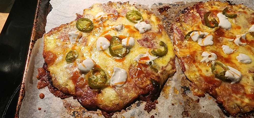 Low carb pizza made on a tortilla with tomato sauce, mozzarella cheese, pepperoni, jalapeños, aoli, and hot sauce.