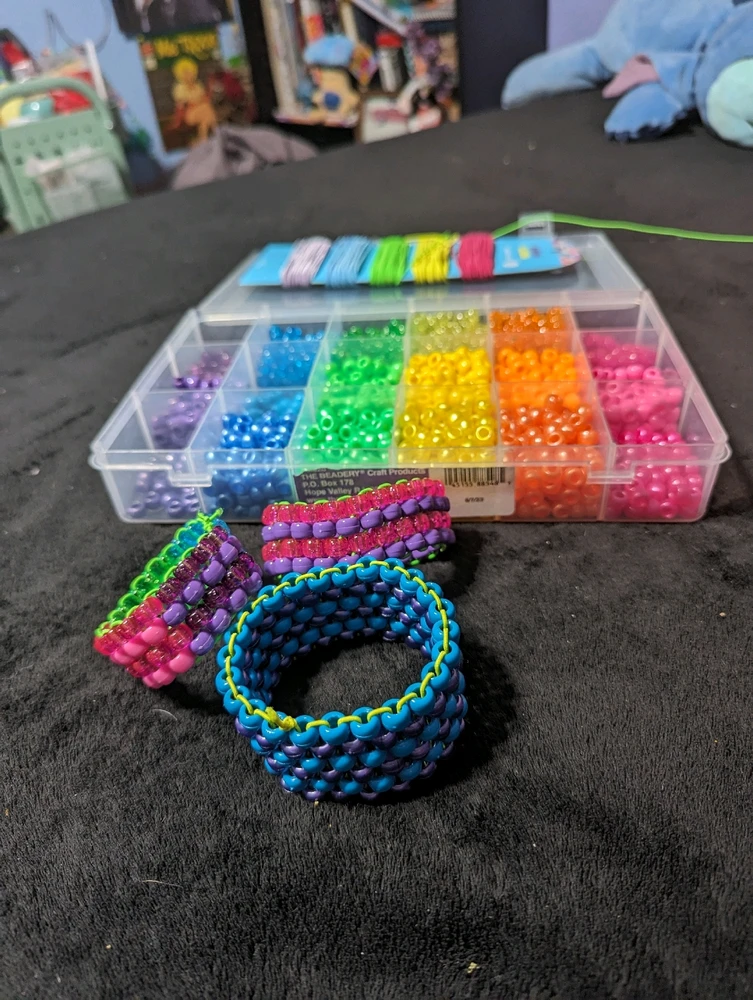 3 beaded rave cuff bracelets in multiple colors and sizes in front of a container of rainbow assorted beads.