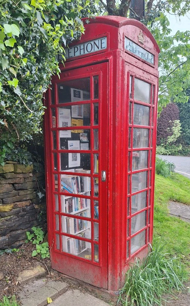 Old British red telephone box used as public library with books inside.