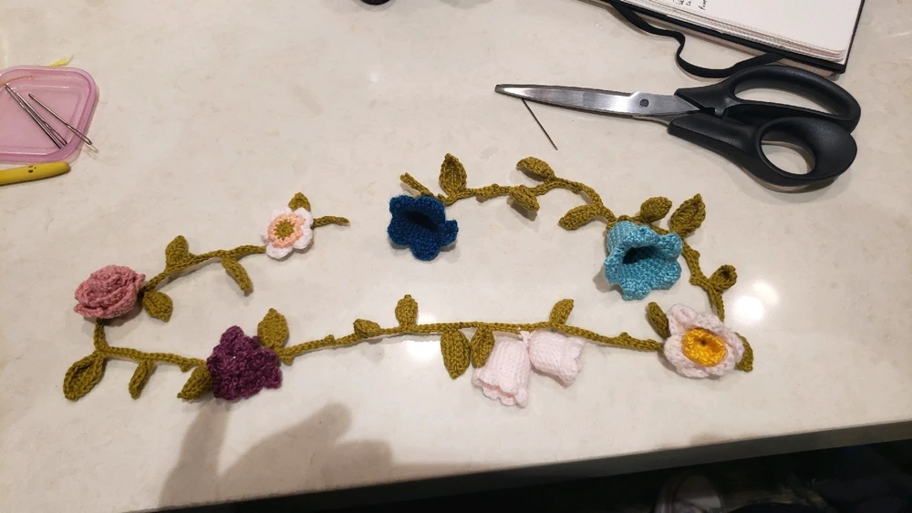 A crochet vine in green with several crochet flowers attached 