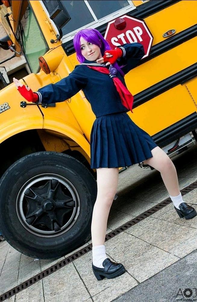 Chica con uniforme escolar japonés azul, pelo lila. Bus escolar amarillo detrás. Ella hace pose de lucha y tiene guantes