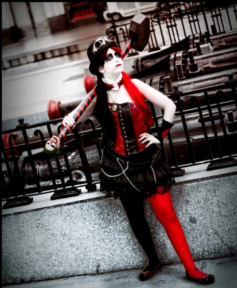 Chica con pelo rojo y negro, cara pintada de blanco que parece un panda. Ropa steampunk roja y negra. Con un mazo
