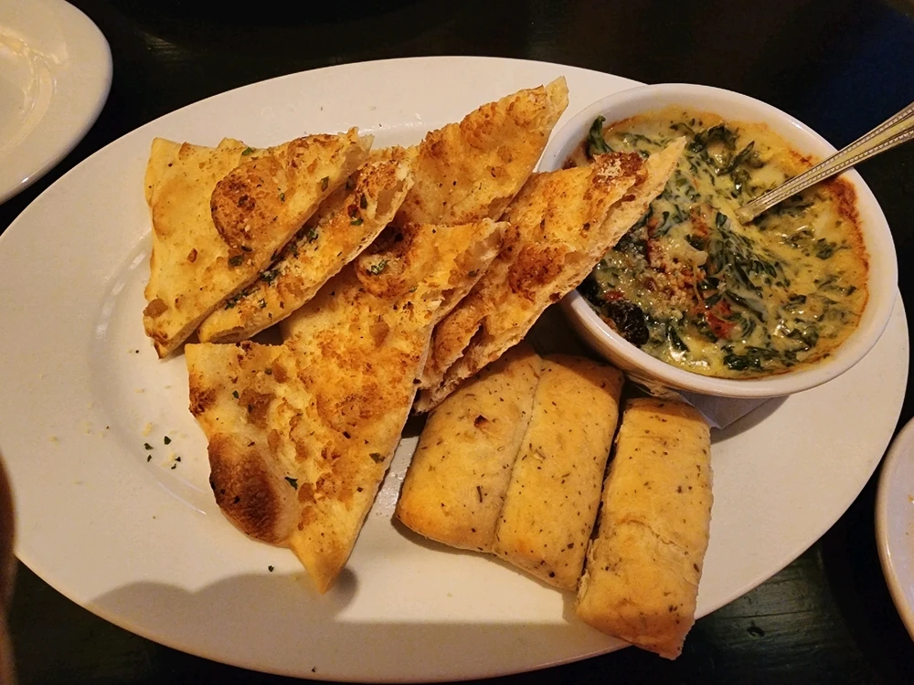 Bread triangles on a plate. A small bowl on the plate with spinach artichoke dip.