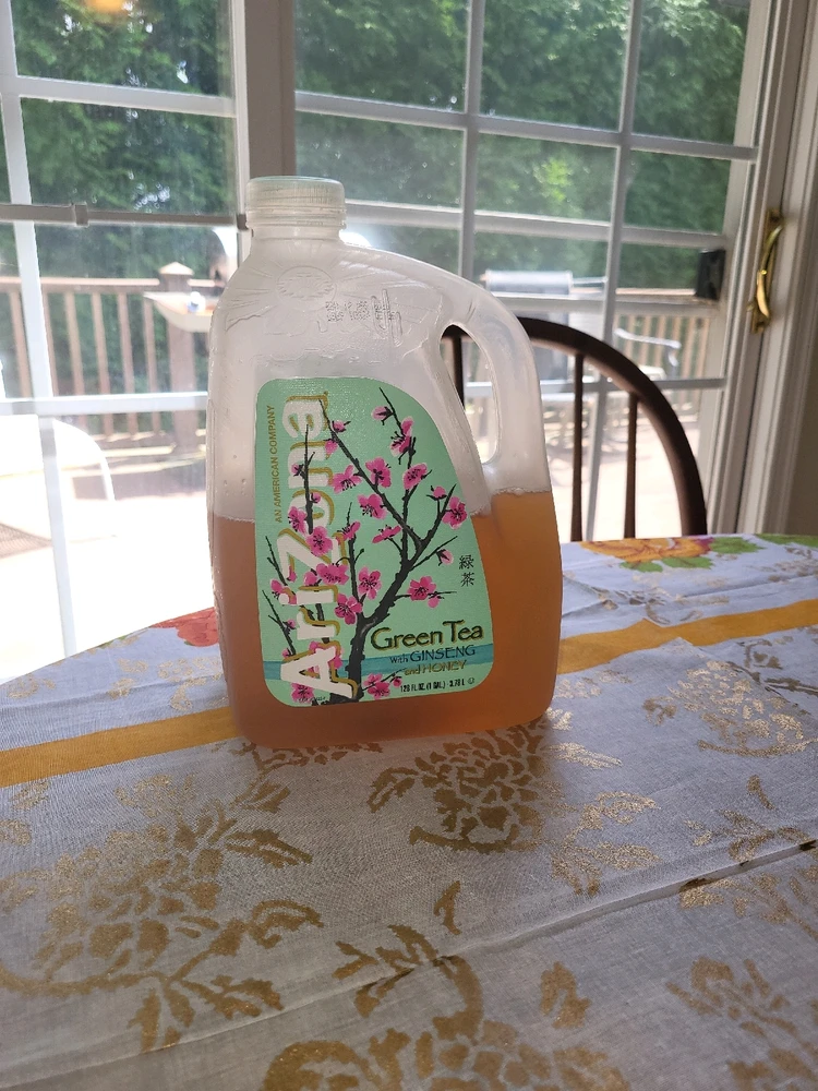 A bottle of Arizona green tea half full on a table.