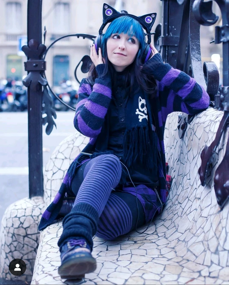 Chica con pelo azul ropa lila y negra y unos auriculares 