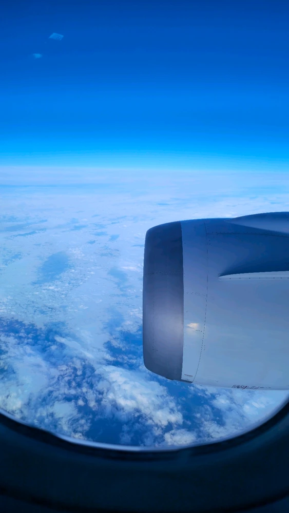 Boeing 787 right side engine through an electrically tinted viewport over clouds 