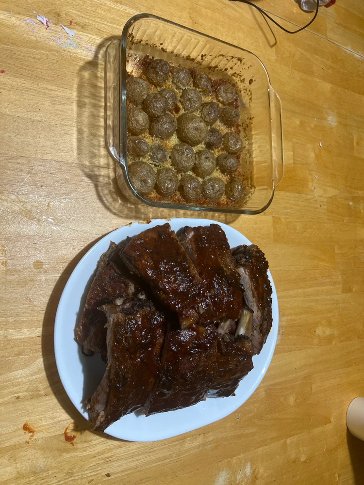 A kitchen table.  On the table sits a glass baking dish with parm crusted potatoes. On a platter sits bbq pork ribs.
