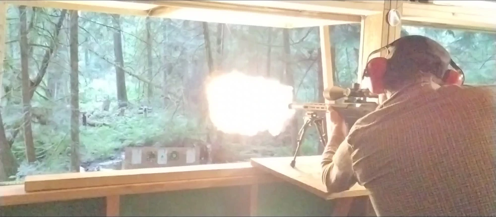Man is firing a rifle at a distant target, the flash from the bullet is a large ball of fire that brightens the whole room.