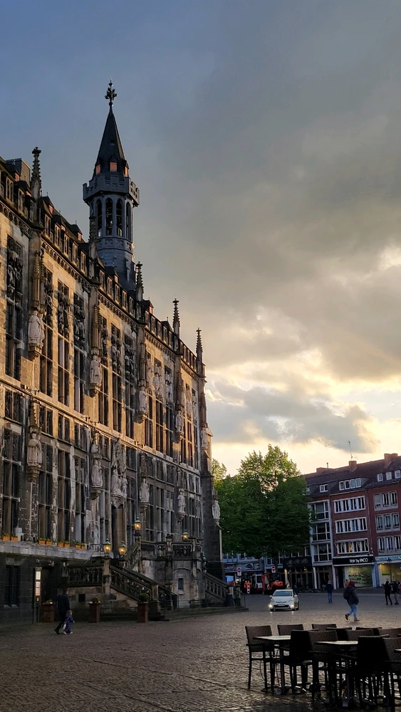 An image of the City Hall in Aachen, Germany. The building is on the left side, with an off-screen sunset illuminating it.