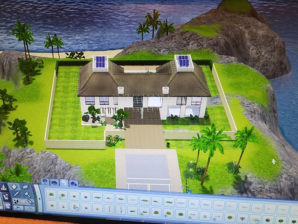 An image of the outside of a modern style house with white walls and brown windows. It's on a mowed lawn and a seaside cliff.