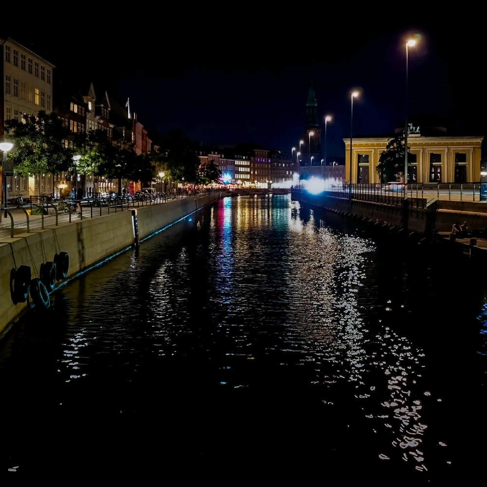 Colored lights at central copenhagen reflect on the surface of the water in the chanel between houses