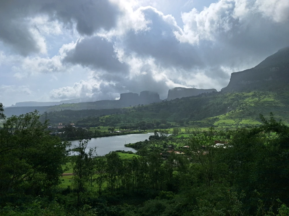 A scenic view of the mist-covered Brahmagiri Hills in Nashik  with lush greenery, a calm lake, and dramatic cliffs.