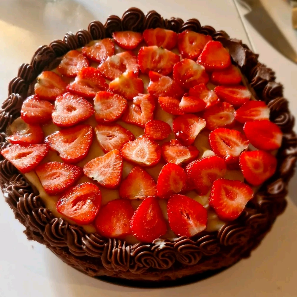 A chocolate cake with caramel sauce, cut strawberries and piped frosting on a white table