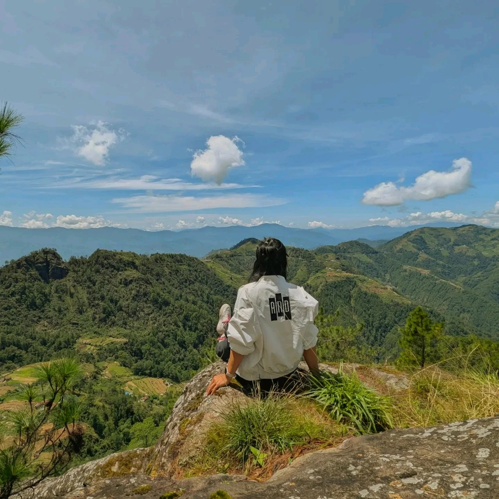 Panoramic view of a mountainous landscape. The scene features a clear blue sky, rolling green hills, and distant mountains.