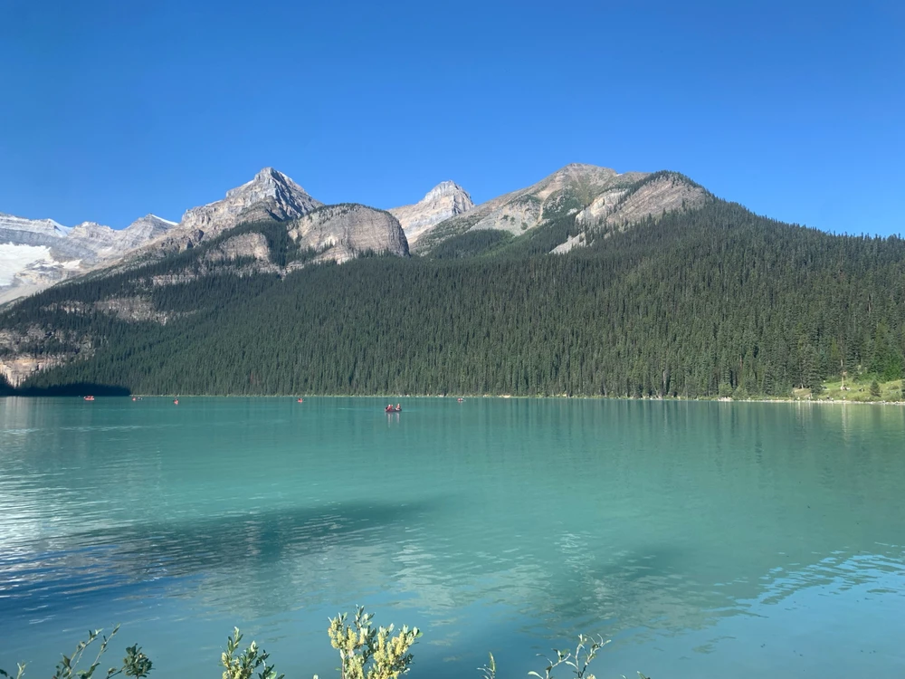 Crystal blue lake with white topped, green mountains in the background. 