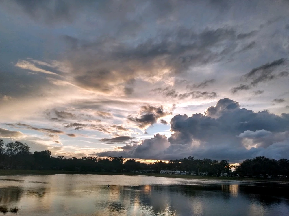 Thick fluffy cloud covering the sun as it sets, hovering over a lake. 