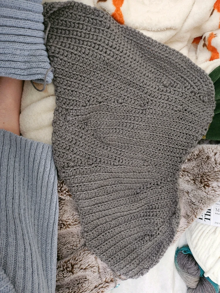 Grey yarn knit together, it starts long but slowly slims down, making the would-be beanie shape uneven. 
