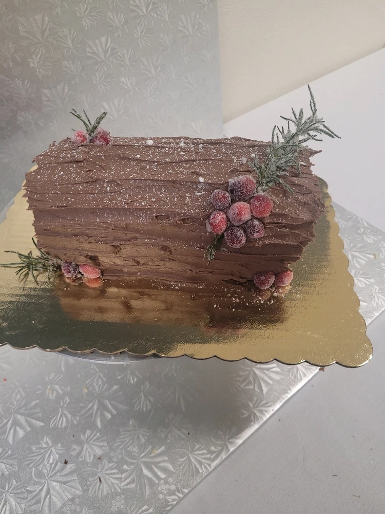Yule log with chocolate buttercream and a chocolate and hazelnut whip filling. Topped with candied cranberries and Rosemary