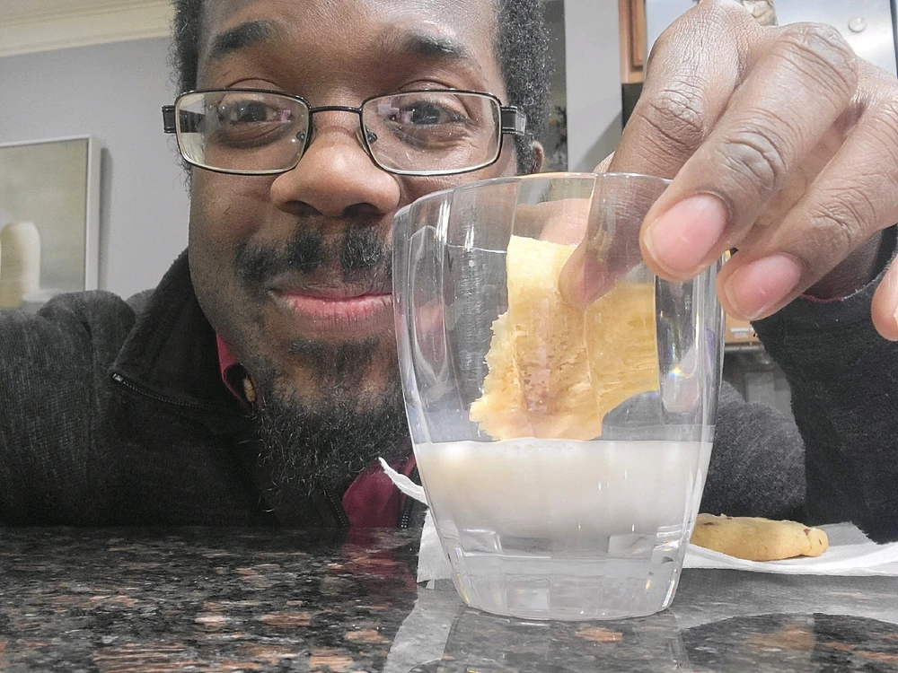 A cool smiling guy dunking a cookie into some almond milk