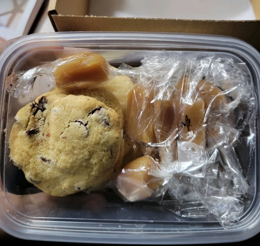 A box of baked goods, on the left is a chocolate chip cookie and on the right are salted caramels!