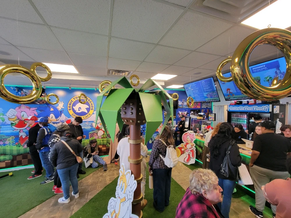 A cafe with the theme of Sonic the Hedgehog, there is a fake palm tree in the middle of the room and floating gold rings.