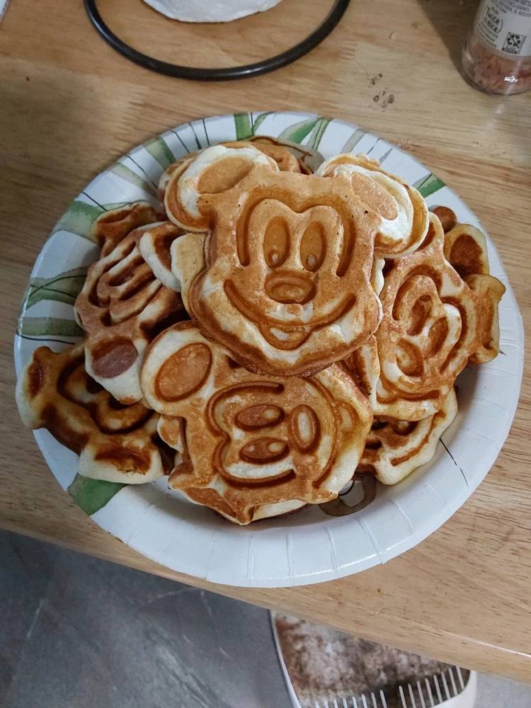 A paper plate with mini waffles shaped like mickey mouse. The waffles are roughly 6 inches. There's a small mound of waffles.