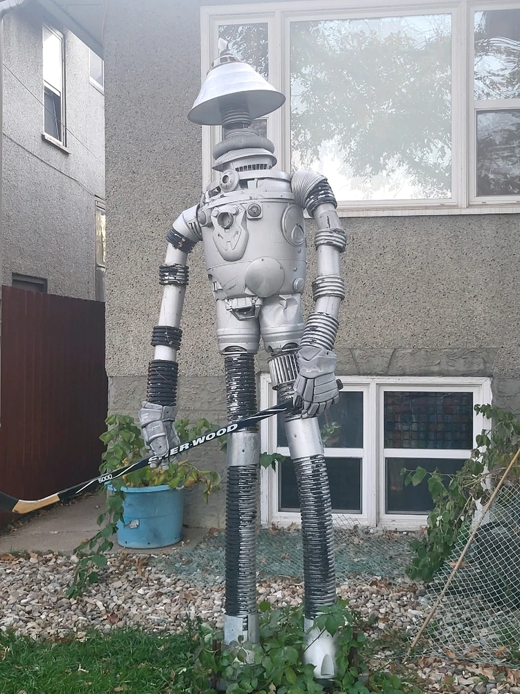 A large sculpture made of repressed electronics painted silver in the shape of a robot holding a hockey stick.