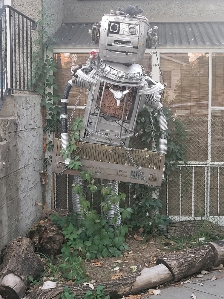 A large sculpture made of repressed electronics painted silver in the shape of a robot playing a keytar.