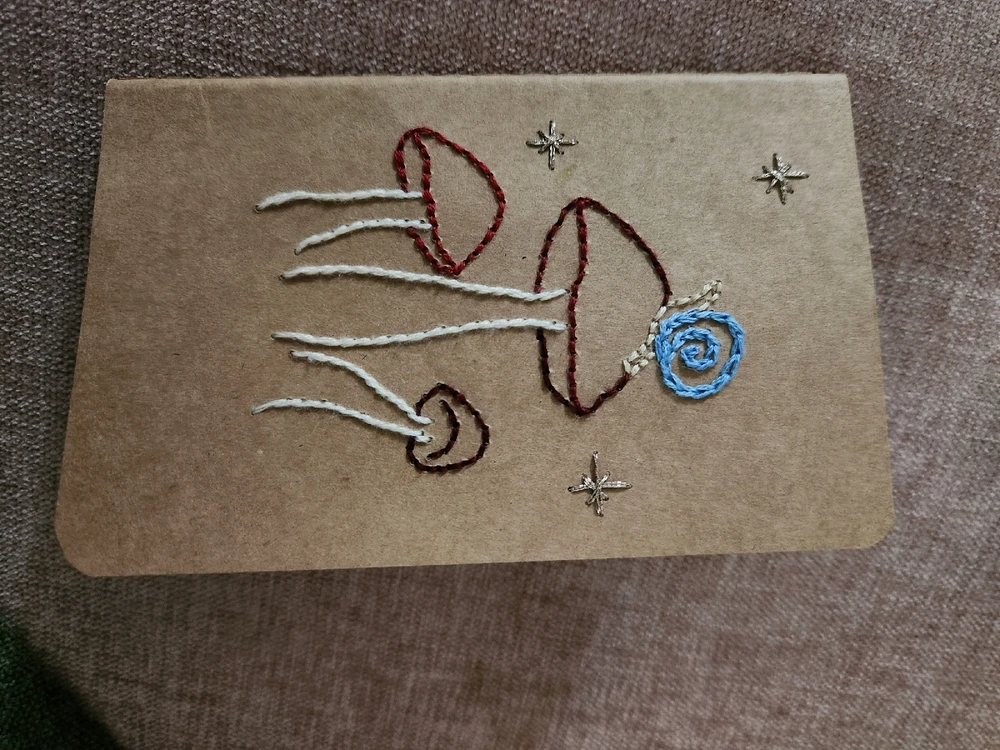 Small, brown paper notebook with three red and white mushrooms in the center. There is a small snail on the central mushroom.