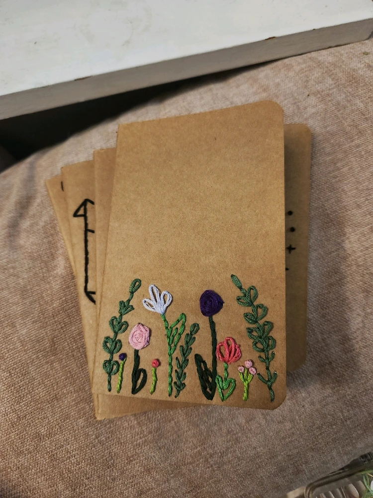 Small, brown paper notebook with flowers embroidered at the bottom of the cover. Main color scheme is pink and purple.