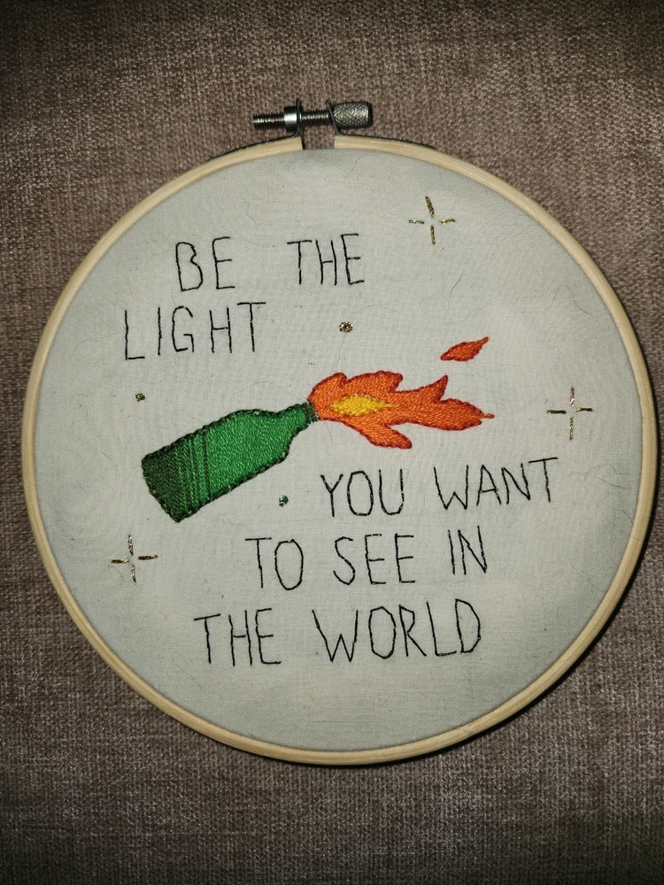 "Be the light you want to see in the world" embroidered around an image of a lit molotov cocktail. Tone indicator: humor